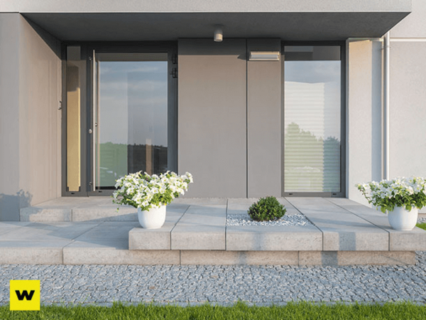Moderner Hauseingang mit großen Fenstern, Steinplatten und Blumenkübeln auf der Terrasse.