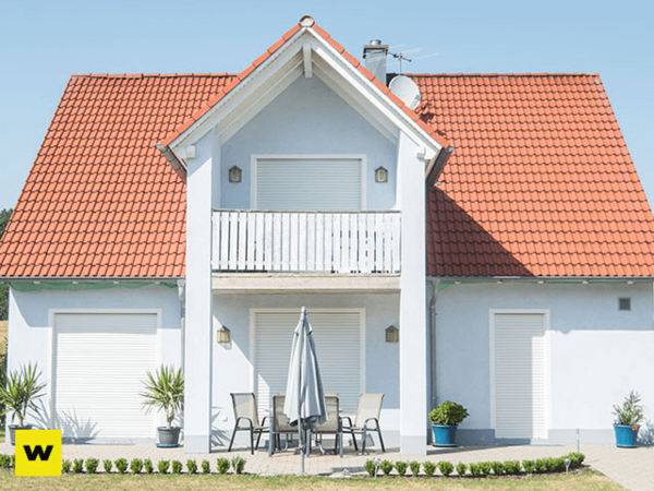 Modernes Einfamilienhaus mit rotem Satteldach, Balkon und Terrasse im Sonnenschein.